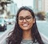 pexels-photo-1239291-1239291 A young woman with glasses smiling on a city street, embracing urban lifestyle.