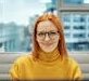 pexels-photo-5917849-5917849 Professional woman with glasses working at an office desk with a cityscape view.